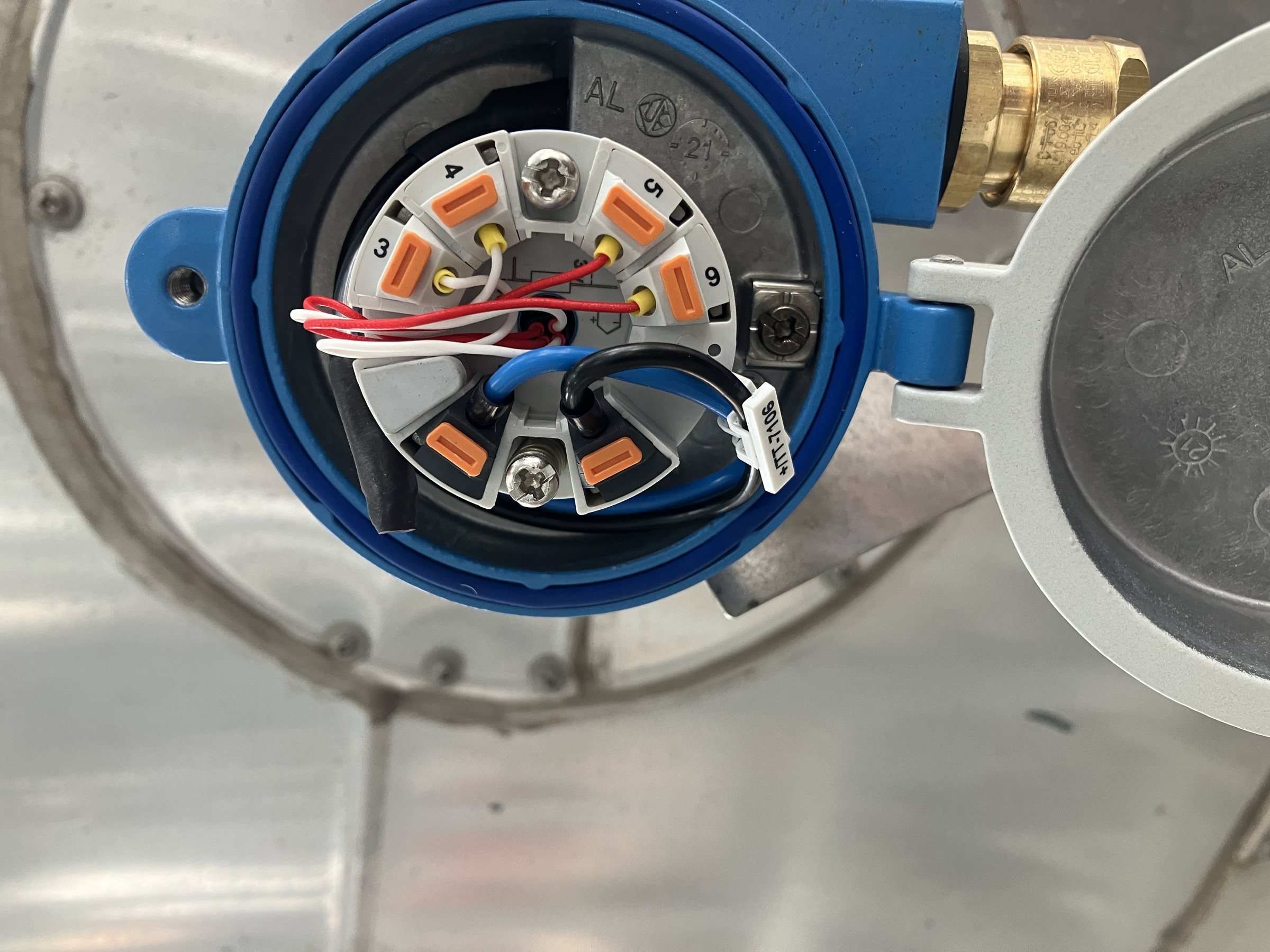 The opened terminal head of a blue process transmitter, showing its wiring and terminal numbering during inspection.